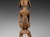 une statue en bois représentant une femme assise sur une table