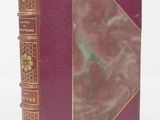 an old book with a red cover sitting on top of a white surface