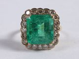 a close up of an emerald and diamond ring on a white surface