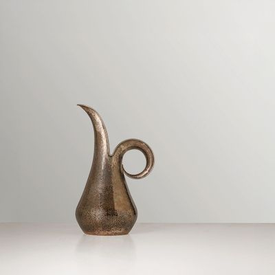 un vase en bronze muni d'une anse incurvée, posé sur une table blanche