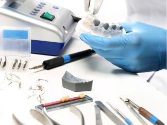 une personne portant un gant bleu et tenant une brosse à dents ainsi que quelques outils