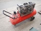 a red air compressor sitting on the ground next to a chair