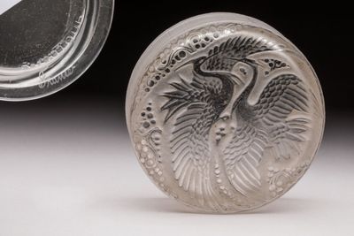 un objet en argent orné d'un oiseau, à côté d'un récipient en verre