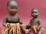 pair of african dolls sitting next to each other on a pink background