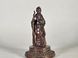 une statue en bronze représentant un homme tenant un bâton, posée sur un socle