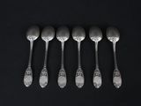 six silver spoons are lined up in a row on a black surface