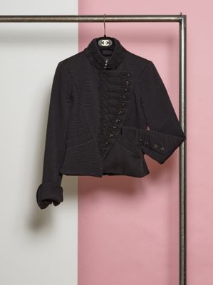 une veste noire suspendue à un porte-vêtements devant un mur rose et blanc