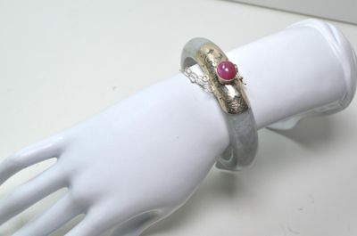 une main de mannequin blanche tenant une bague sertie d'une pierre rouge
