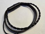 un gros plan d'un bracelet en cuir noir posé sur une surface blanche