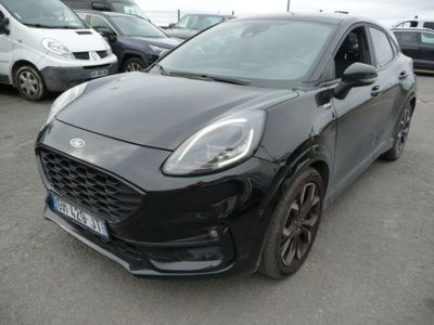 La voiture noire est garée sur un parking, avec d'autres voitures en arrière-plan.