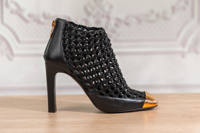 La chaussure à talons hauts noire et dorée est posée sur une table en bois