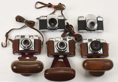 six appareils photo sont alignés sur une surface blanche, maintenus par des lanières en cuir