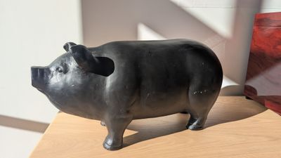 statue d'un cochon assis sur une table en bois, à côté d'un sac rouge