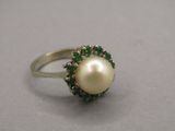 une image représentant une bague ornée d'une perle et d'une émeraude sur un fond gris