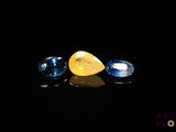 two blue and one yellow sapphires on a black surface