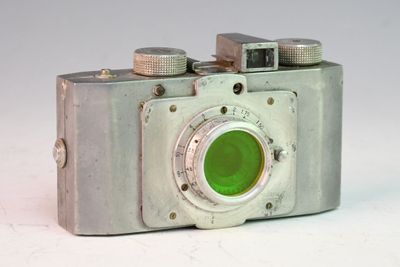 un appareil photo argenté avec un objectif vert posé sur une surface blanche