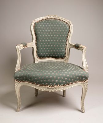 une vieille chaise dont l'assise est recouverte d'un tissu vert et blanc