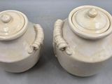 two white vases with handles sitting on a table