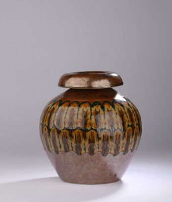 un vase marron et noir muni d'un couvercle, posé sur une surface blanche