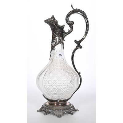 un pichet ancien en argent et en verre posé sur un socle, sur fond blanc