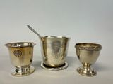 three silver cups and spoons sitting next to each other on a table