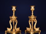 a pair of antique brass candlesticks on pedestals on a dark background