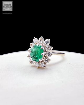 un gros plan d'une bague sertie d'une émeraude verte et de diamants, posée sur une assiette blanche