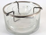 a clear glass container with a metal handle on a white surface