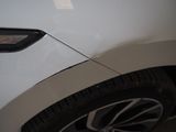 the front end of a white car with a dent on it ' s bumper