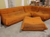 un grand canapé orange et un pouf dans une pièce
