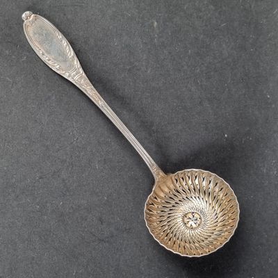 une cuillère en argent ancienne posée sur une surface noire, avec une cuillère en argent au milieu