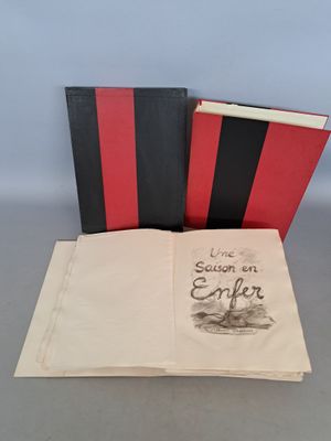 un livre ouvert posé sur une table, à côté d'un livre rouge et noir
