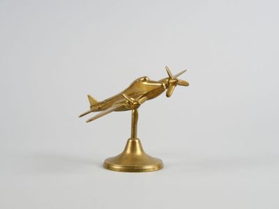 figurine d'avion dorée posée sur un socle, sur fond blanc