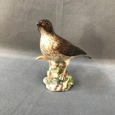 une petite figurine représentant un oiseau perché sur un morceau de bois