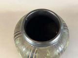 a black vase with a green design sitting on a white surface