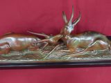 une sculpture en bronze représentant deux antilopes couchées sur un socle en bois