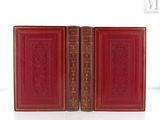 Deux livres rouges aux tranches dorées sont posés sur une surface blanche.