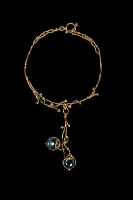 a close up of a gold bracelet with a blue bead