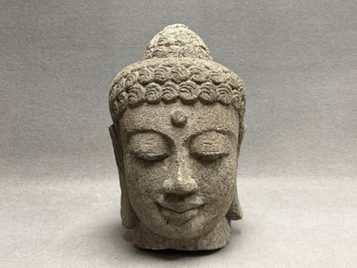 statue représentant une tête de Bouddha aux yeux fermés sur fond gris