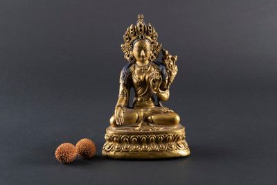 statue en laiton représentant une personne assise sur un socle, avec une noix posée devant elle