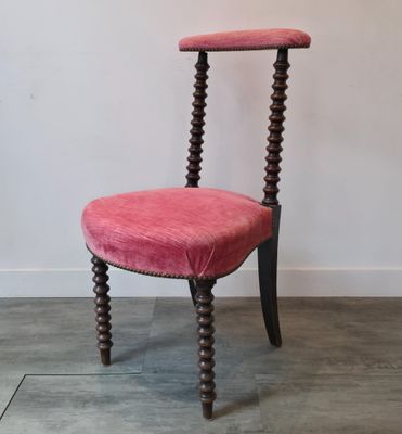 une chaise rose posée sur un parquet, près d'un mur blanc
