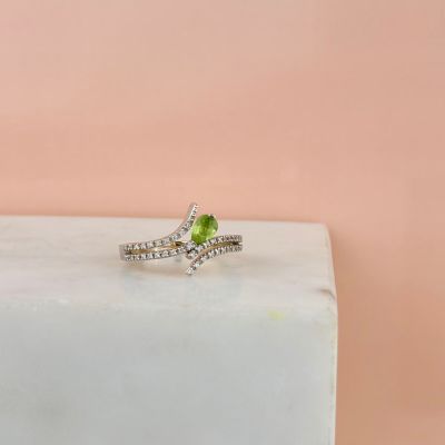 une bague en tourmaline verte et diamants posée sur un bloc de marbre