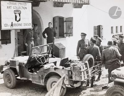 a group of men standing in front of an old jeep