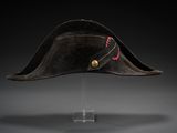 un chapeau noir orné d'un ruban rouge, posé sur un socle transparent