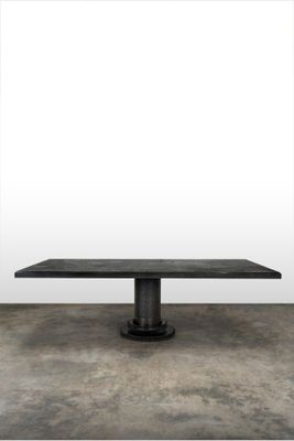 une photo montrant une table noire posée sur un sol en béton, avec un mur blanc en arrière-plan