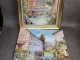 deux tableaux encadrés représentant une rivière et un bâtiment, posés sur une table