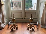two gold candles sitting on a wooden floor in front of a window
