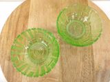 two green glass bowls sitting on top of a wooden cutting board