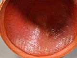 a red vase with a handle on a gray surface