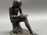 bronze statue of a boy sitting on a rock reading a book